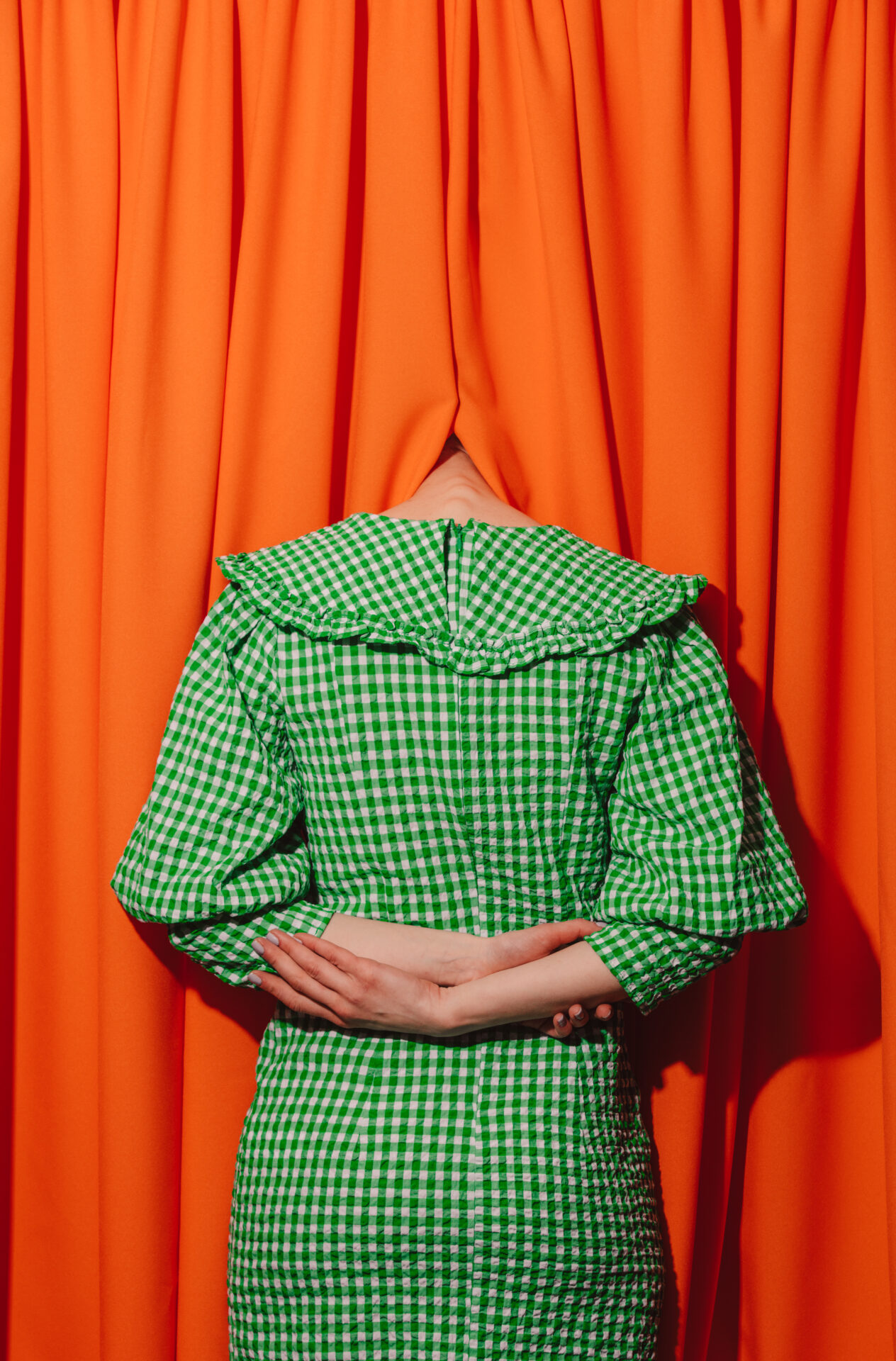 girl in a green dress hides her head in orange curtains